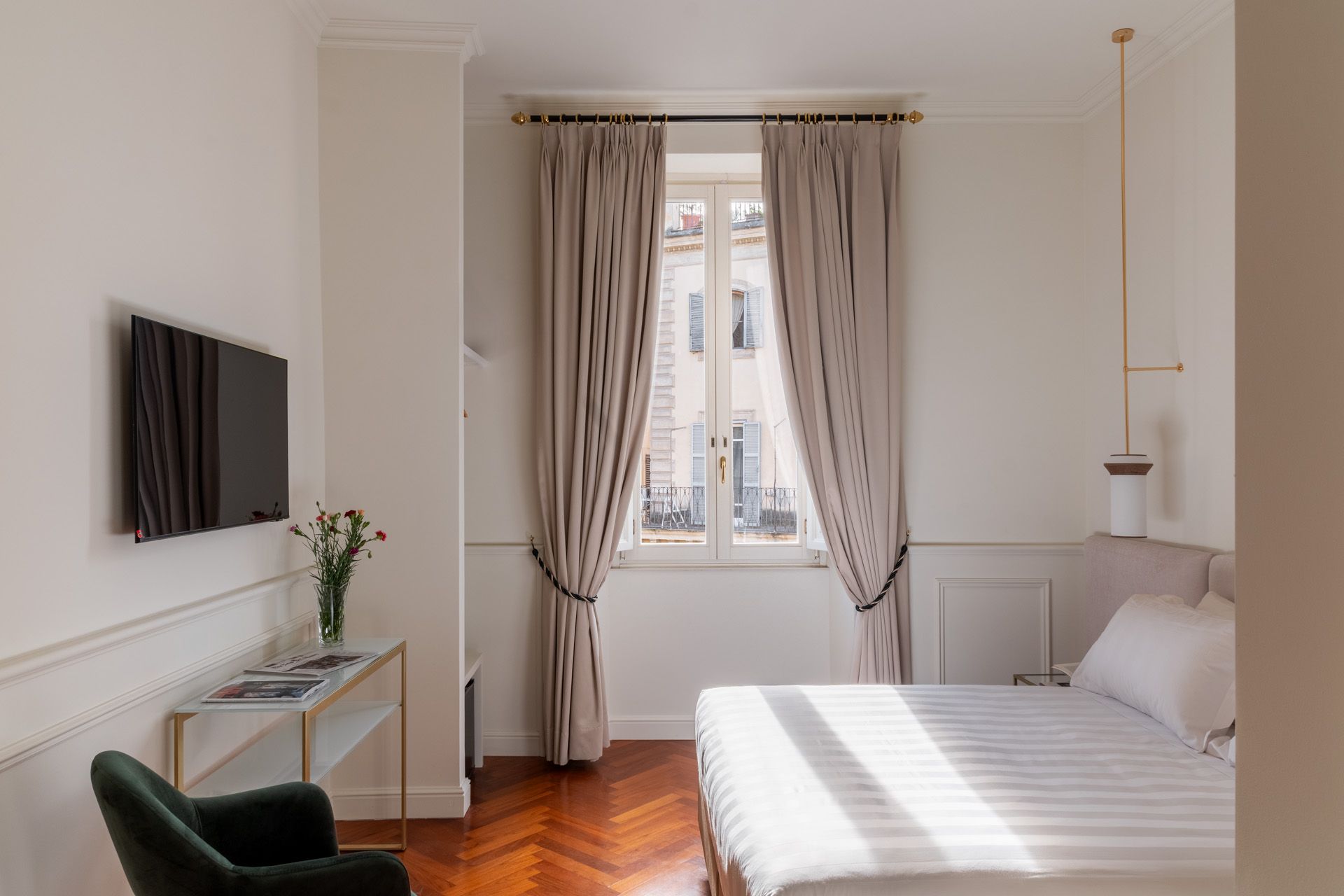 Bedroom with a bed, window with curtains, TV on wall, and a side table with a chair.