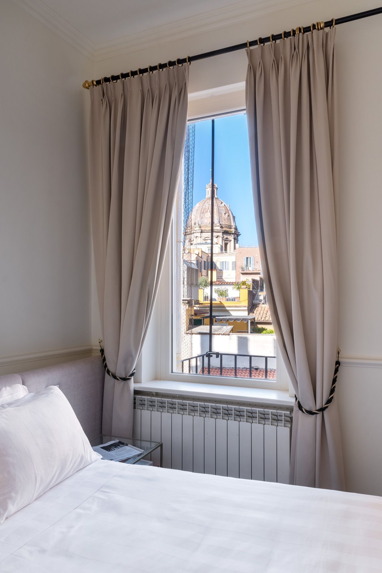 Bedroom window with draped curtains; view of a domed building in a sunny, urban setting.