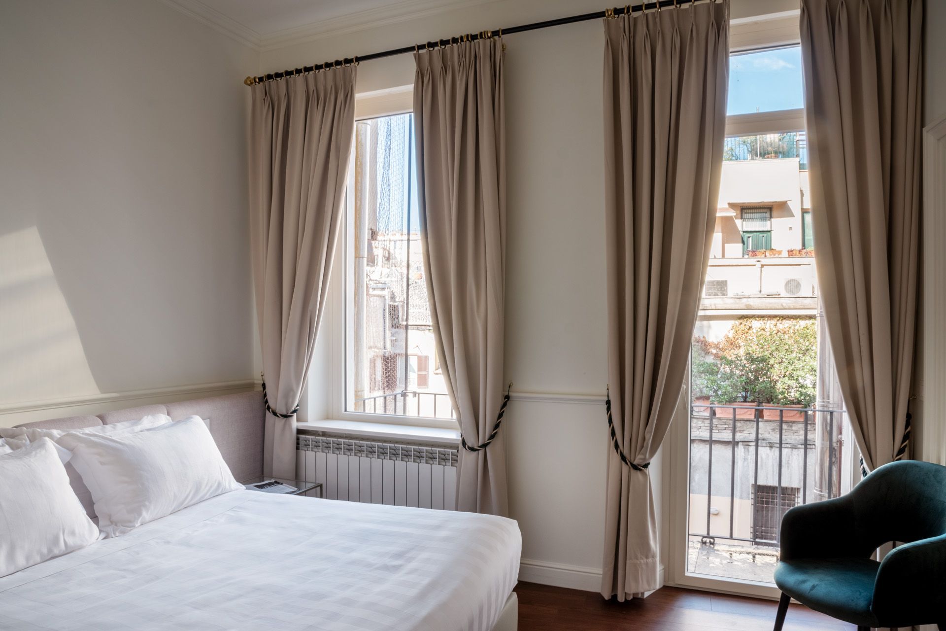 Bedroom with bed, windows with beige curtains, balcony view, teal armchair.