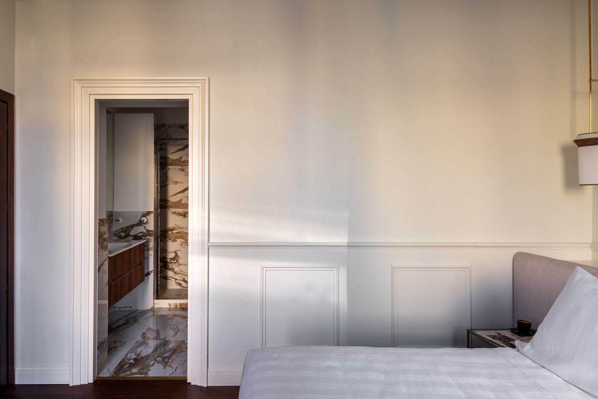 Bedroom with open doorway to bathroom; white walls, patterned floor, wood accents.