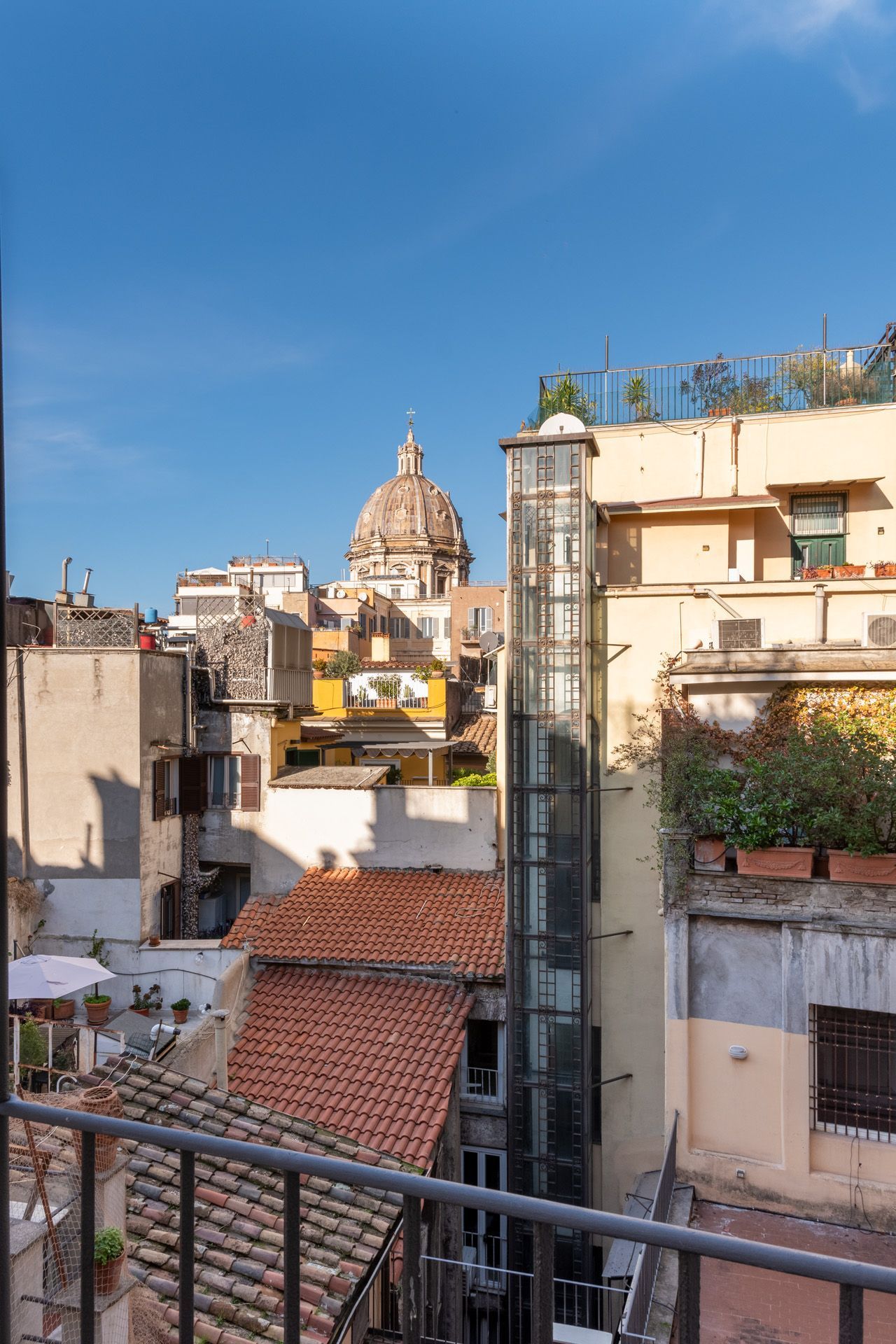 Cityscape with buildings, visible dome, elevator shaft, red tile roof, and a clear blue sky.