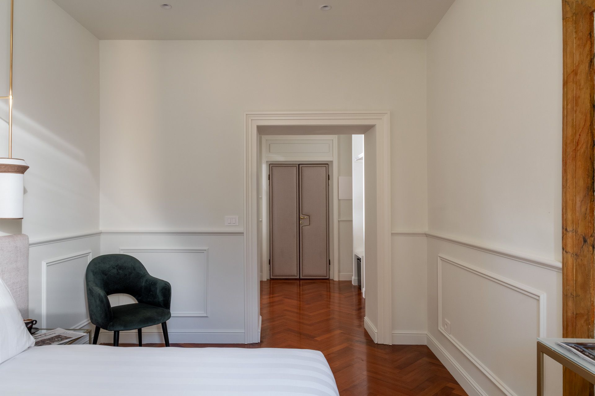 Bedroom with a green armchair, white walls, and a doorway leading to a hallway with closed doors.