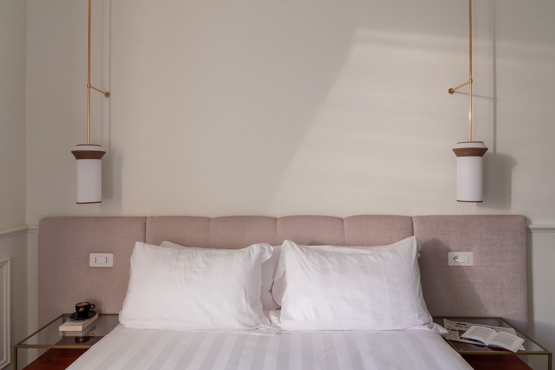 Bedroom with a bed, two white pillows, pink headboard, and two bedside lamps.