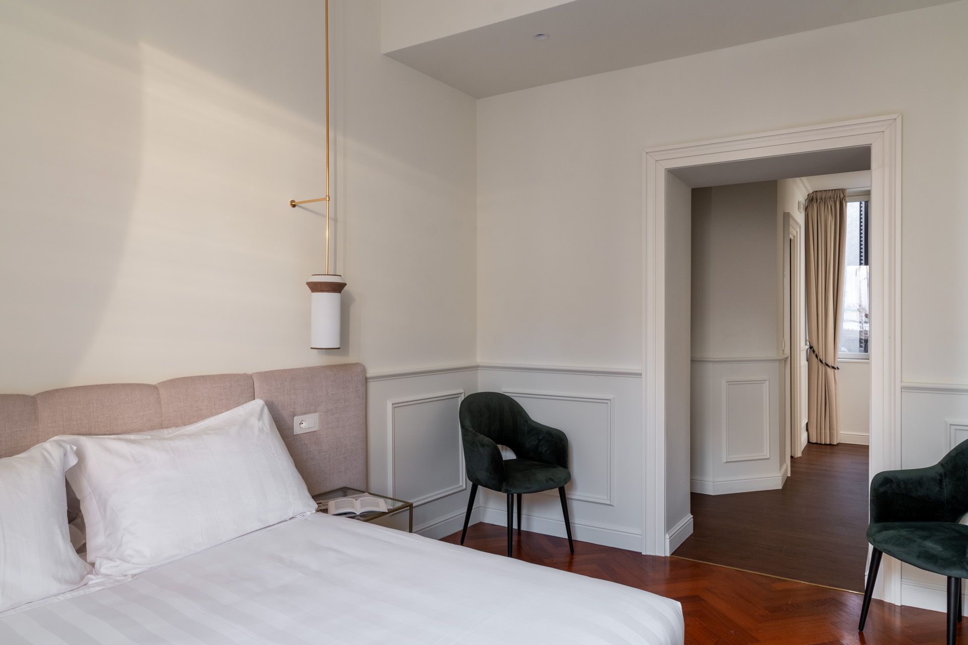Bedroom with bed, velvet chairs, white walls, and doorway.
