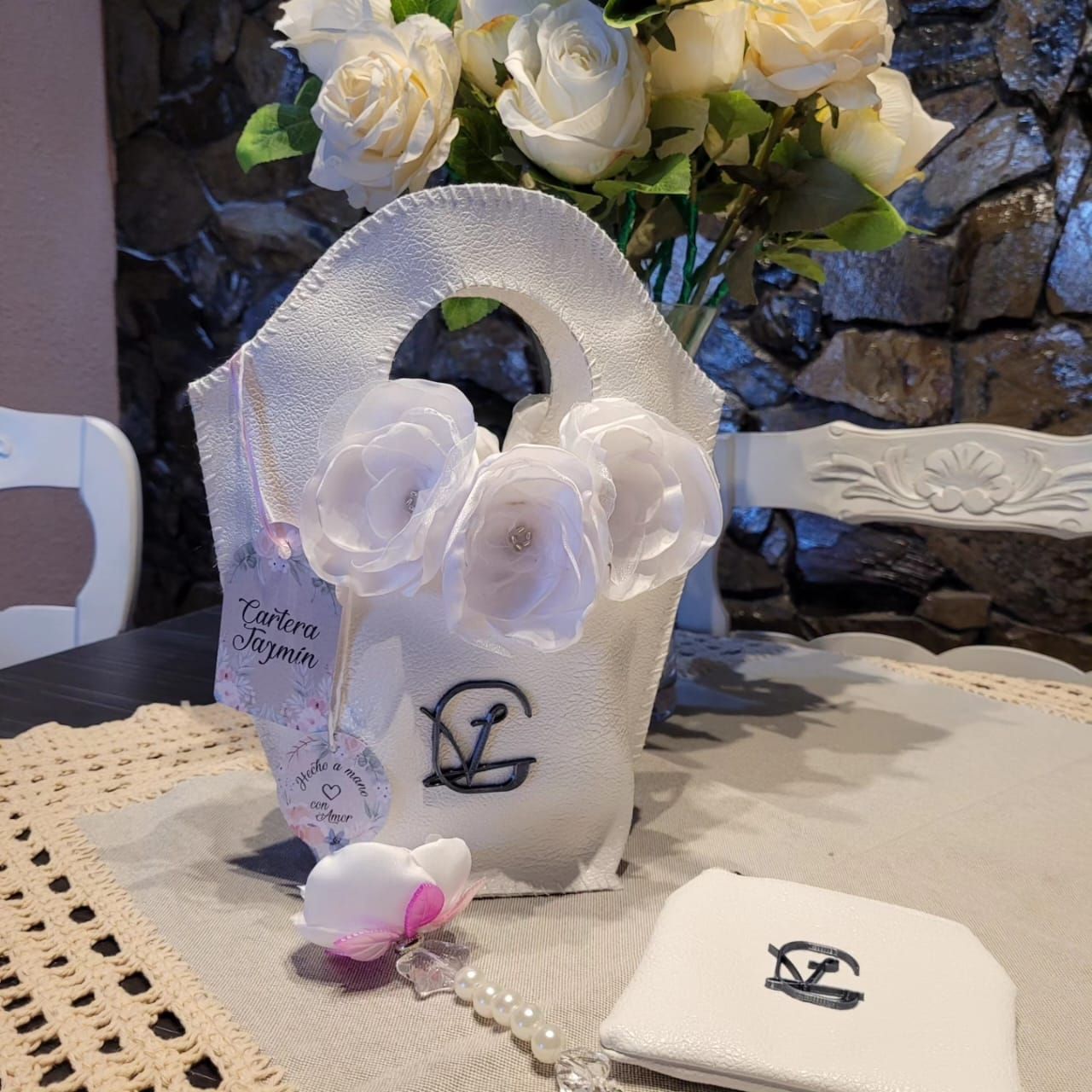 Una bolsa blanca con la letra g está sobre una mesa junto a un jarrón de flores.