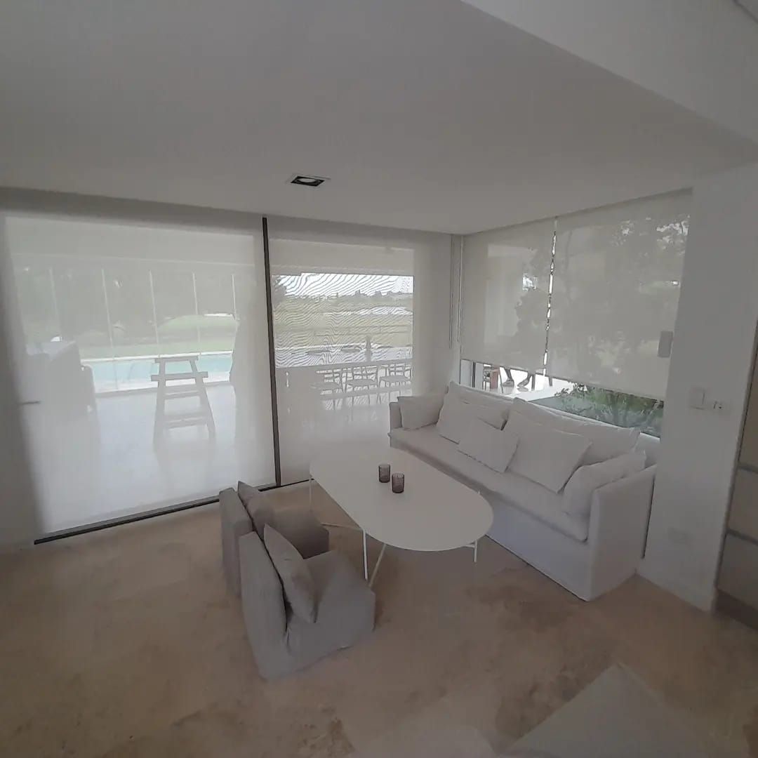 Un salón minimalista con un sofá blanco, dos sillones gris claro y una mesa de centro ovalada sobre un suelo de piedra clara.