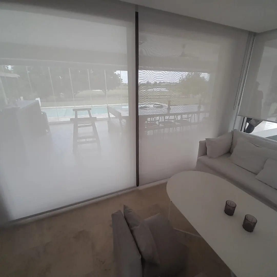 Un salón minimalista con un sofá blanco, una mesa redonda y grandes ventanales con vistas a una piscina y un patio.