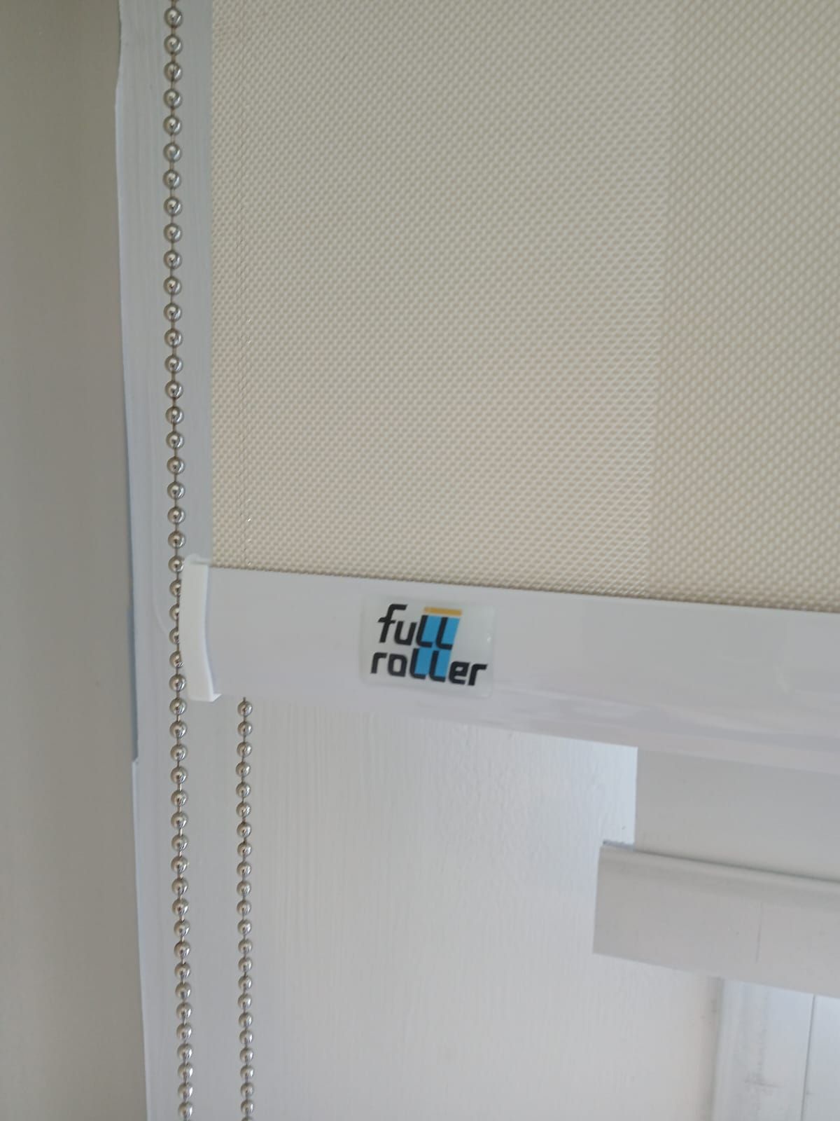 Primer plano de una persiana enrollable blanca con una cadena de cuentas y una etiqueta de la marca