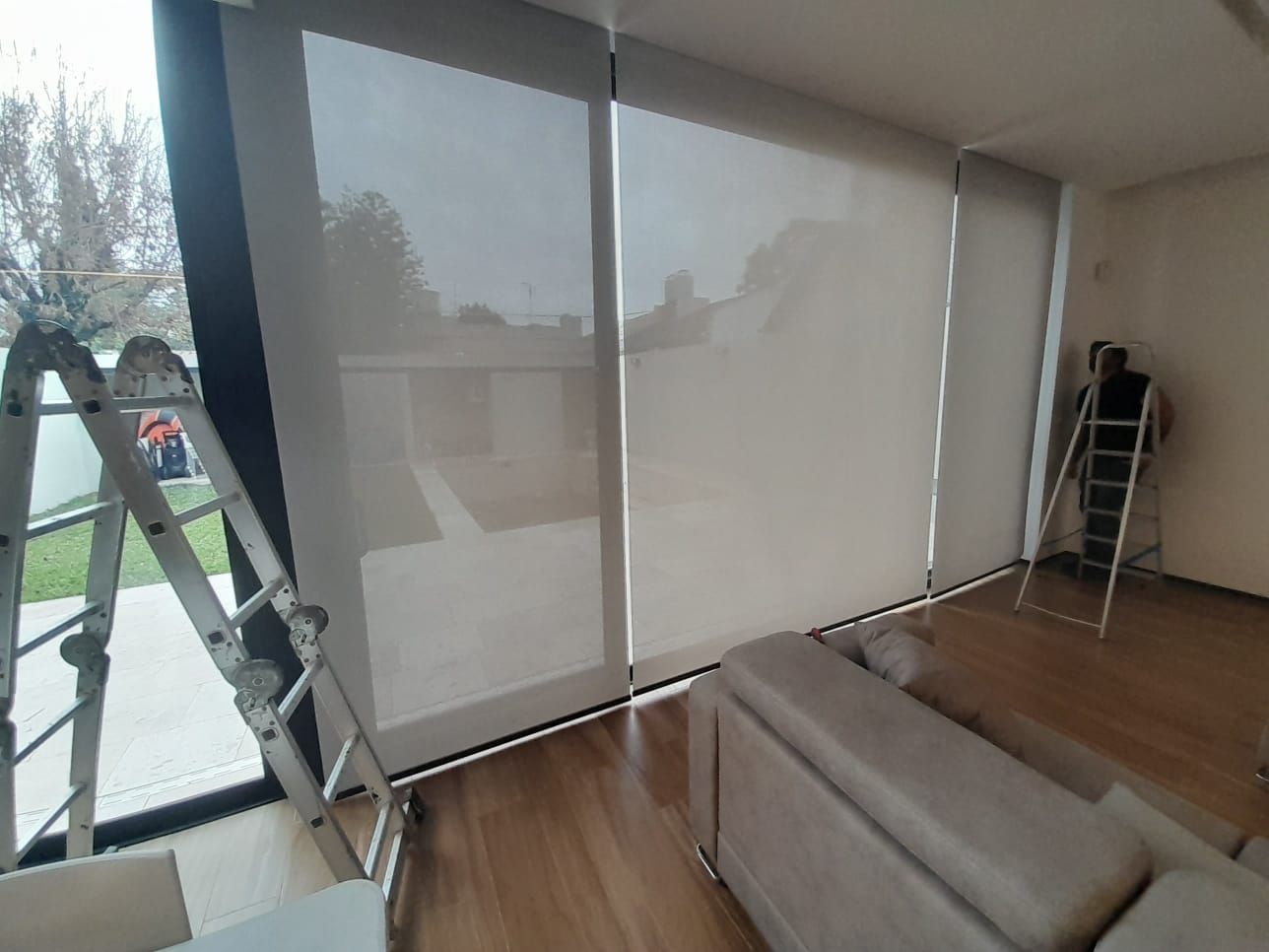 Una persona subida a una escalera instala estores enrollables grises