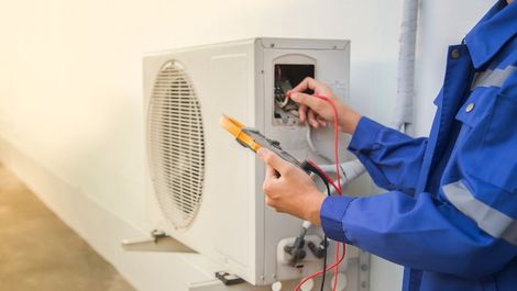 Technician testing an outdoor HVAC unit with a multimeter and wires open.