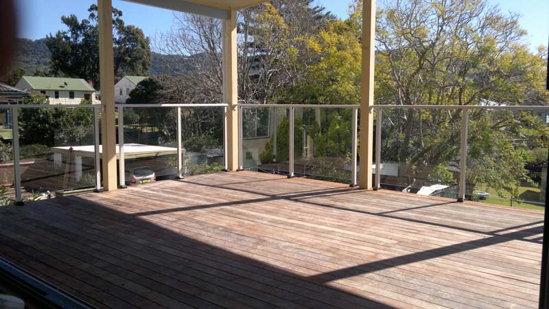 Wooden deck with a glass railing and trees in the background — Balustrading in Unanderra NSW