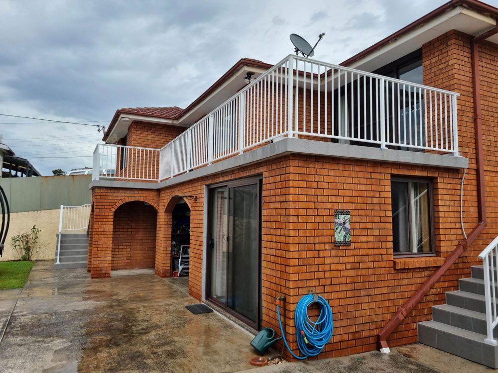 Man in a yellow shirt stands on a set of stairs in front of a house — Pool Fence in Unanderra NSW