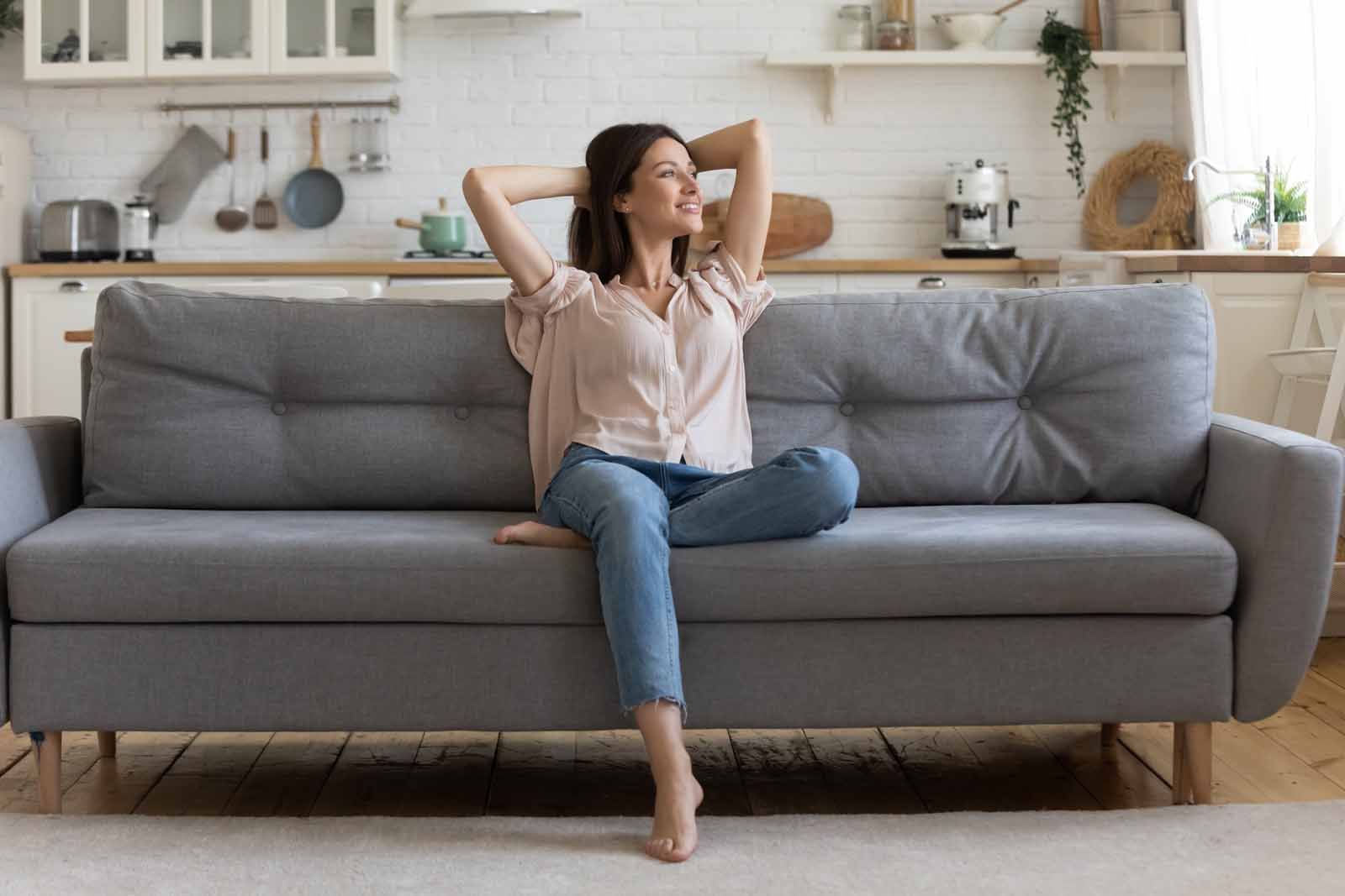 A woman is sitting on a couch in a living room with her legs crossed.