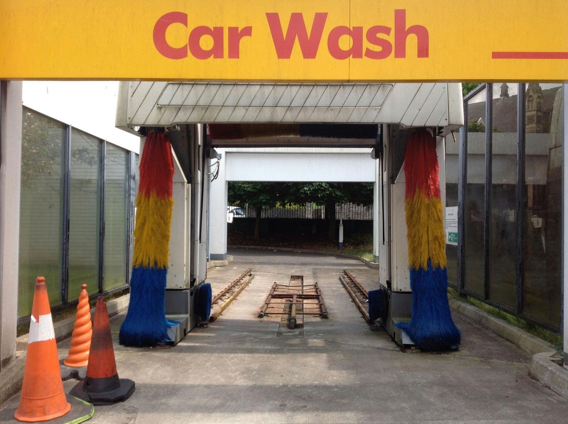 Shell car wash entrance with yellow awning, colorful brushes, and orange cones.