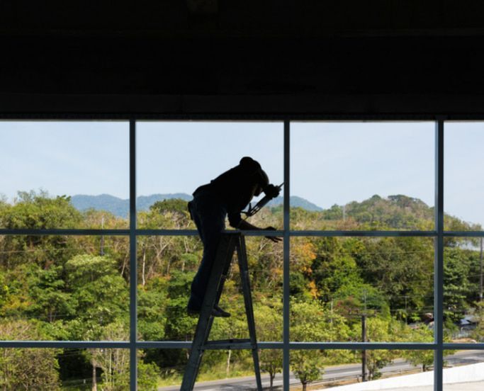 A Man is Standing on a Ladder Cleaning a Window — TSR Tinting & Frosting in Noosa, QLD