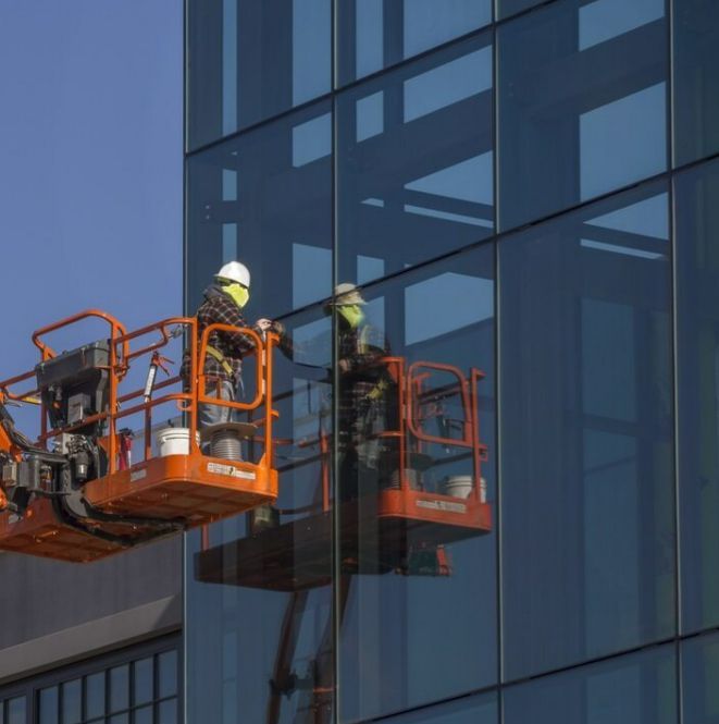 A Man Cleaning a Building With a Lift That Says Jlg on It — TSR Tinting & Frosting in Noosa, QLD