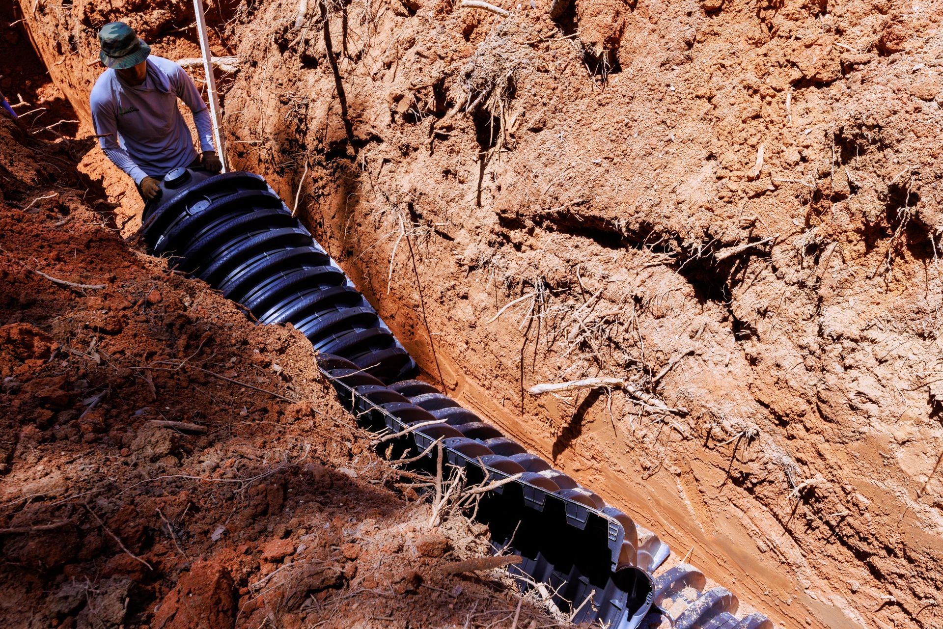 Worker lays black drainage pipe in a red dirt trench