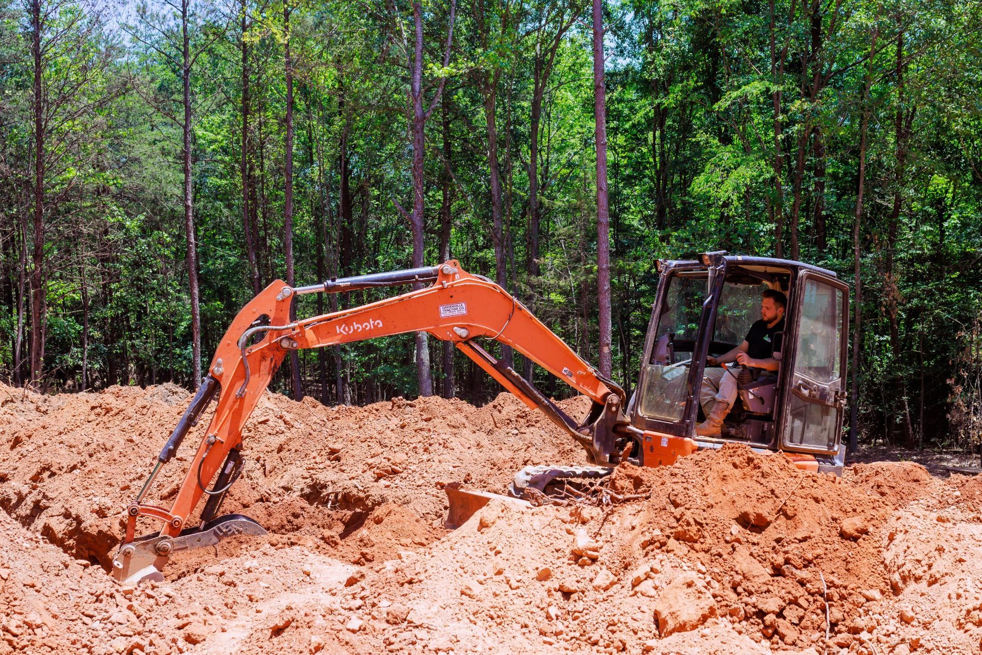 Orange excavator digging through thick mud in a wooded area