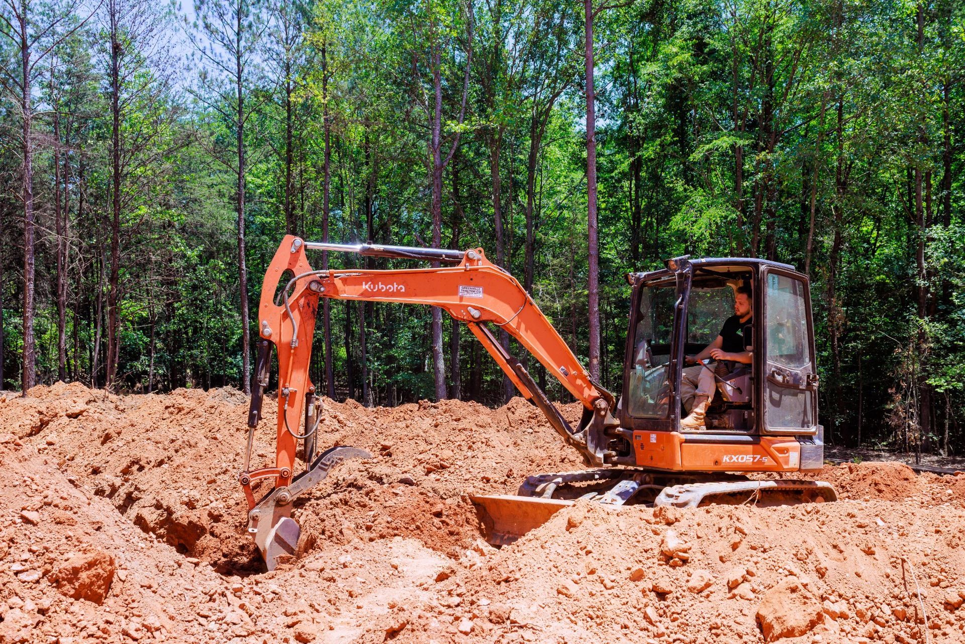 Orange excavator digging dirt at a construction site with a forest in the background