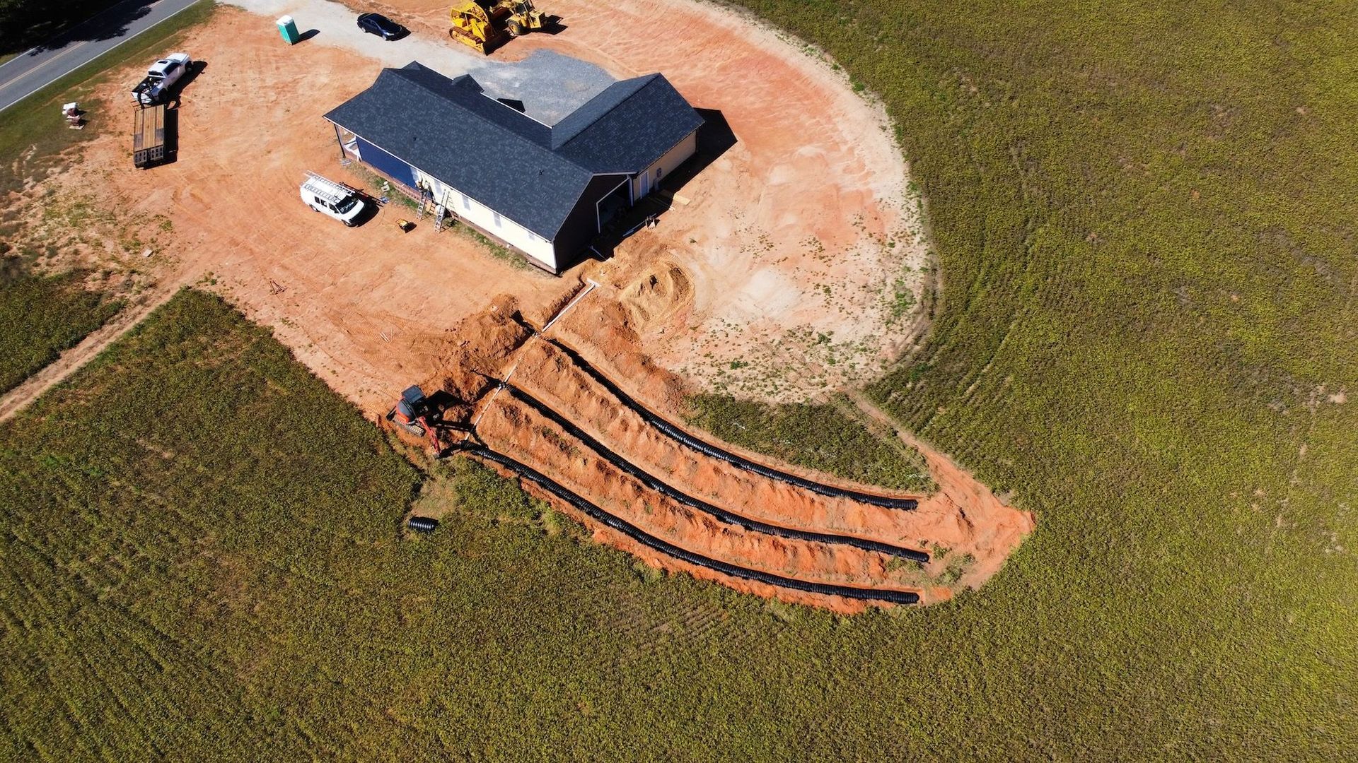 An aerial view of a new house with trenches dug in the grassy yard for a septic drain field installation.