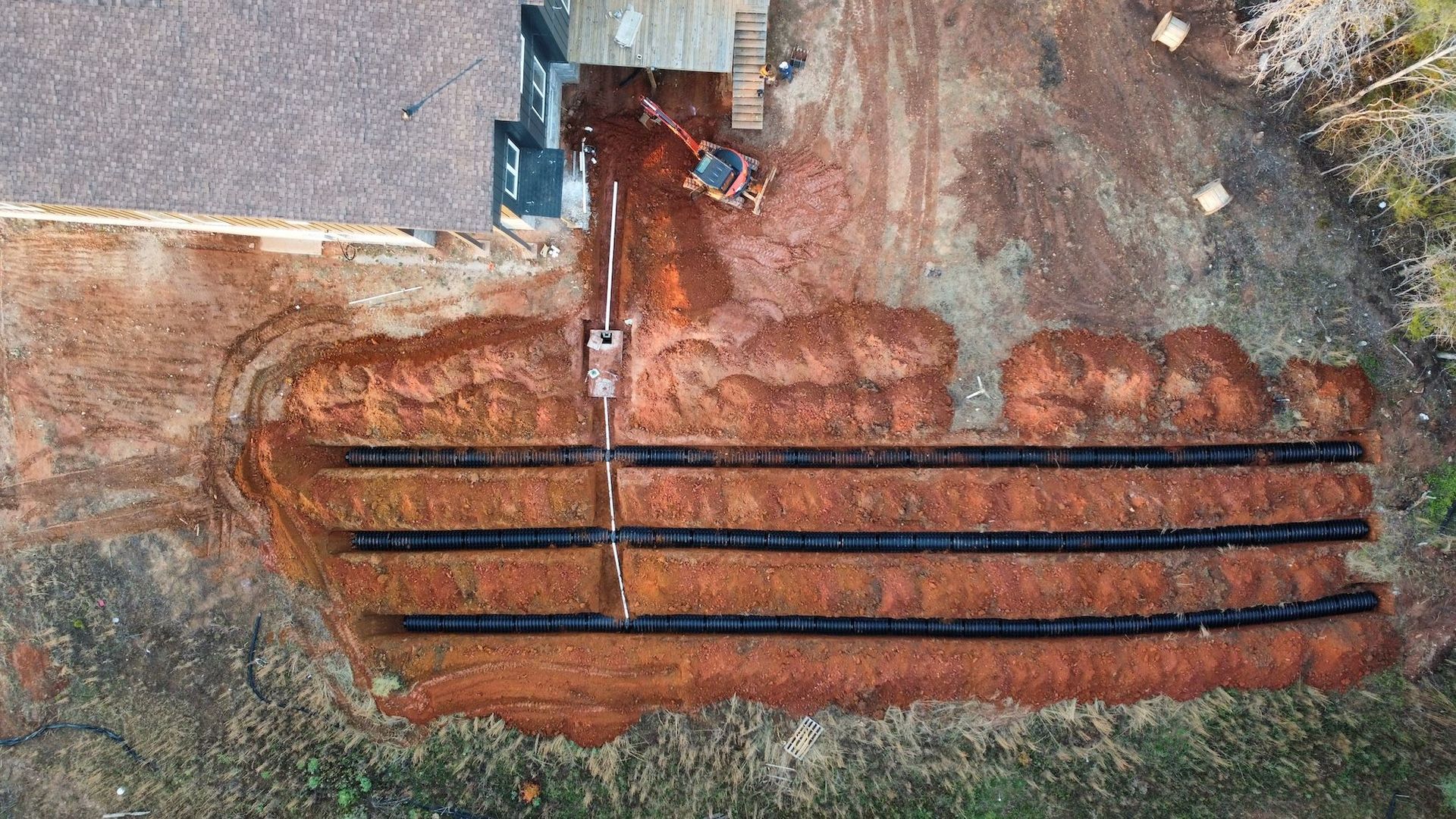 Aerial view of a residential septic system installation with three black drainage lines laid in trenches beside a house.