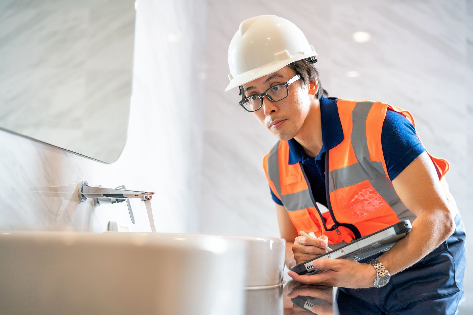 Construction worker in safety gear inspecting a bathroom sink.