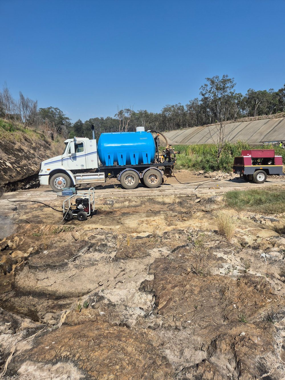 White and Blue Tanker Truck on Rocky Ground With a Red Trailer— TP Concreting In Warilla, NSW