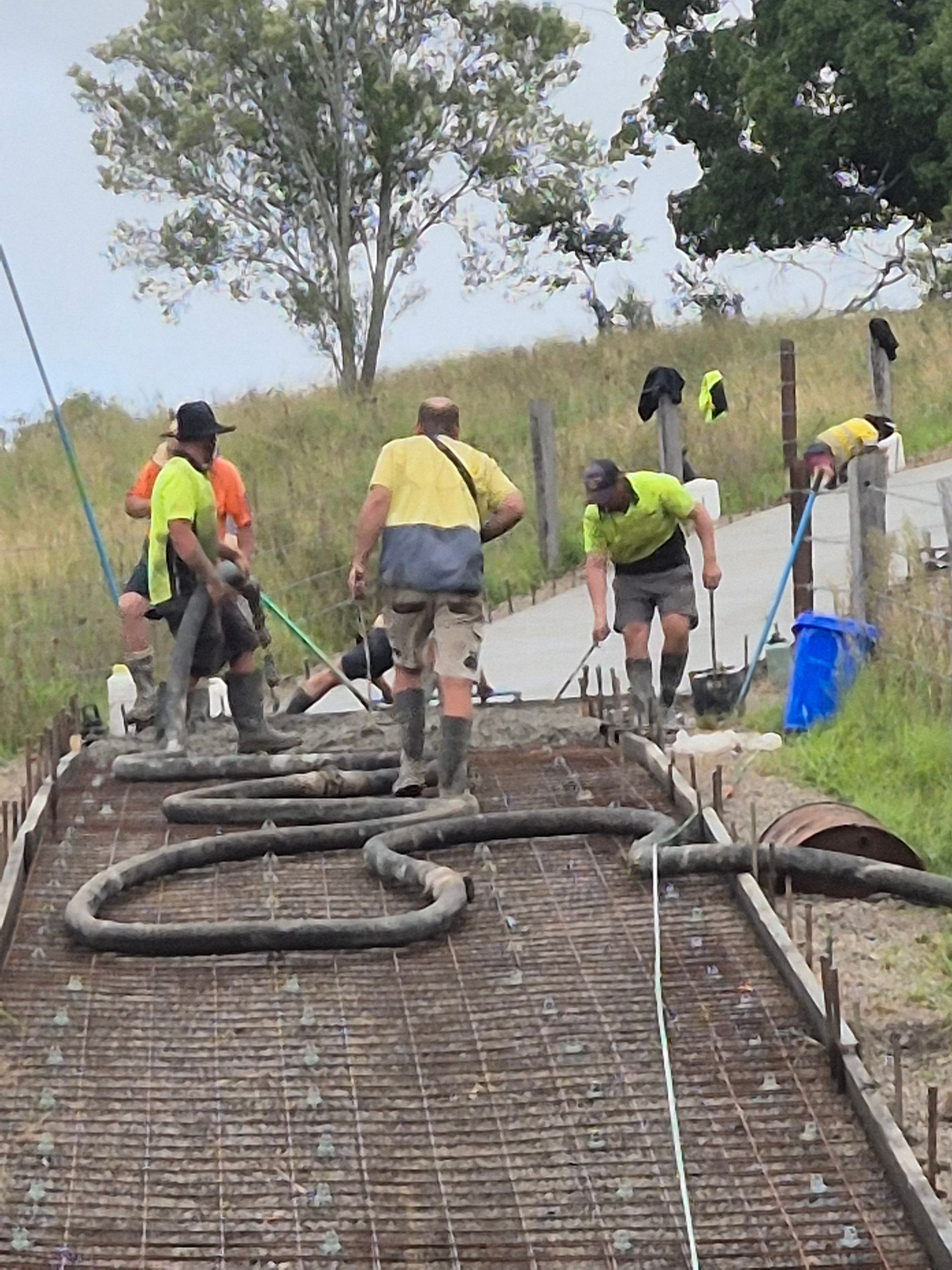 Workers in Neon Safety Vests Pour Concrete on a Rural Road Project — TP Concreting In Warilla, NSW