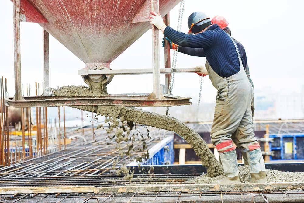 A Man Is Pouring Concrete Into A Concrete Mixer At A Construction Site — TP Concreting In Albion Park, NSW