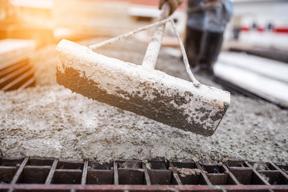A Person Is Pouring Concrete Into A Bucket On A Construction Site — TP Concreting In Shellharbour, NSW