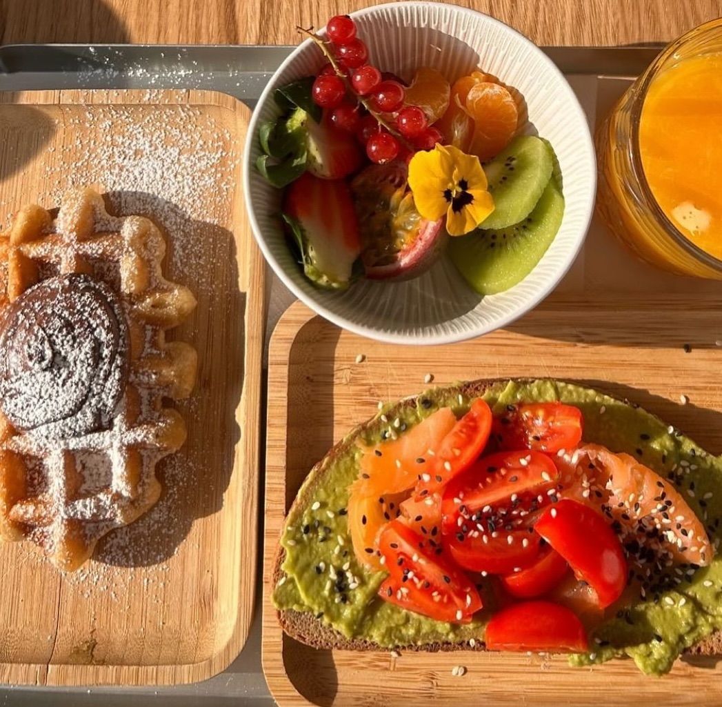 Un vassoio di cibo che include un waffle, un panino e una ciotola di frutta