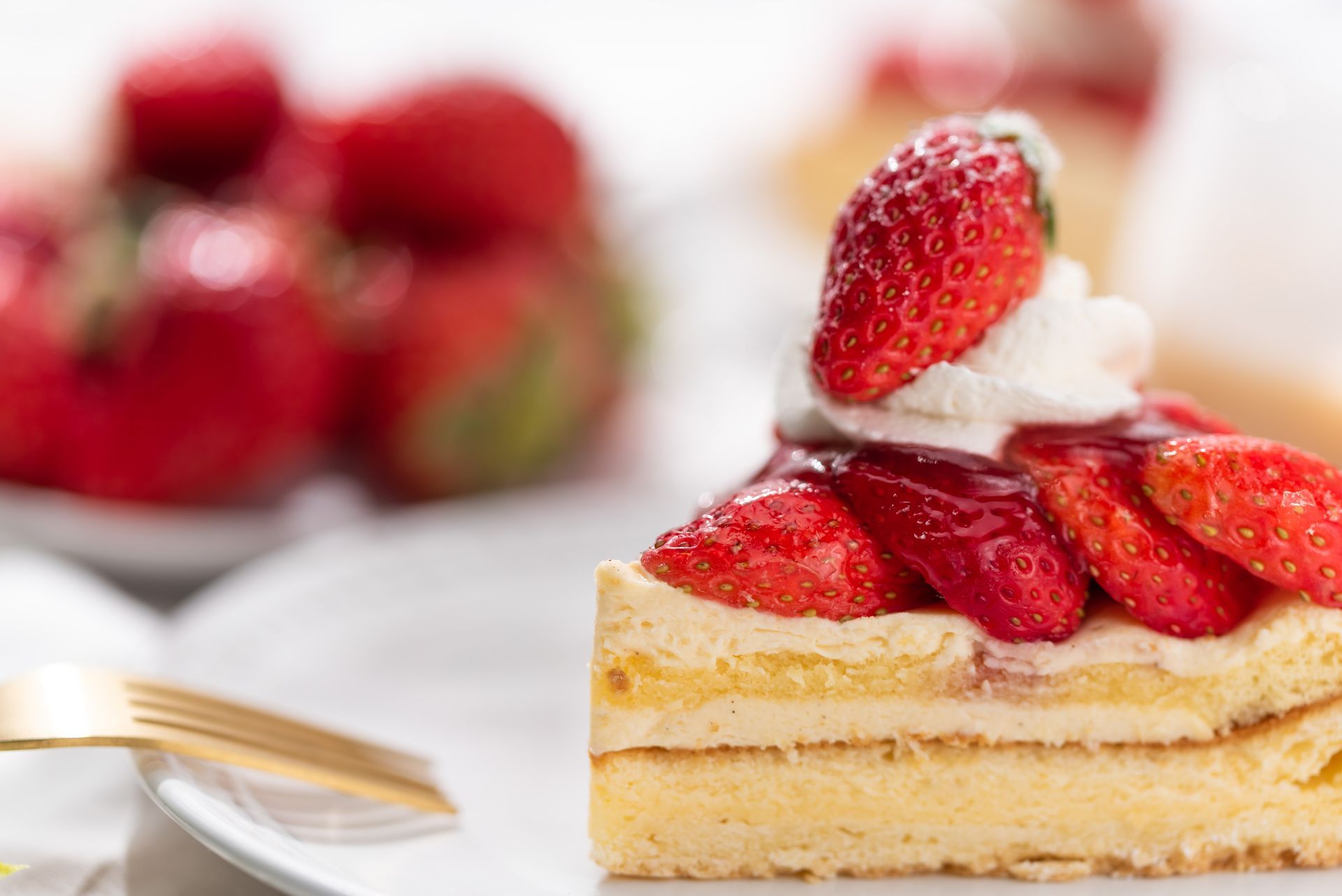 Una fetta di torta con fragole e panna montata su un piatto con fragole sullo sfondo.