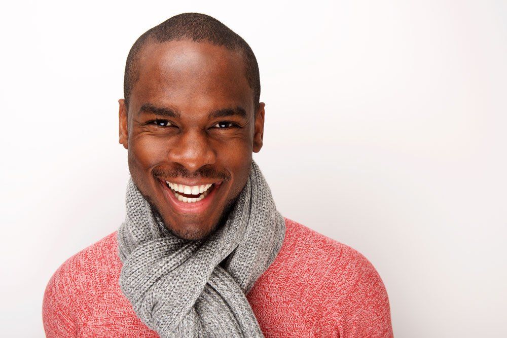 A man wearing a red sweater and a gray scarf is smiling.