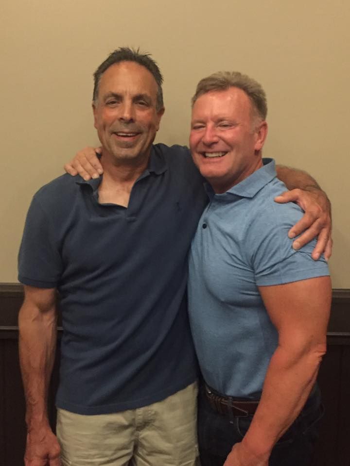 Two men are posing for a picture and one has his arm around the other 's shoulder.