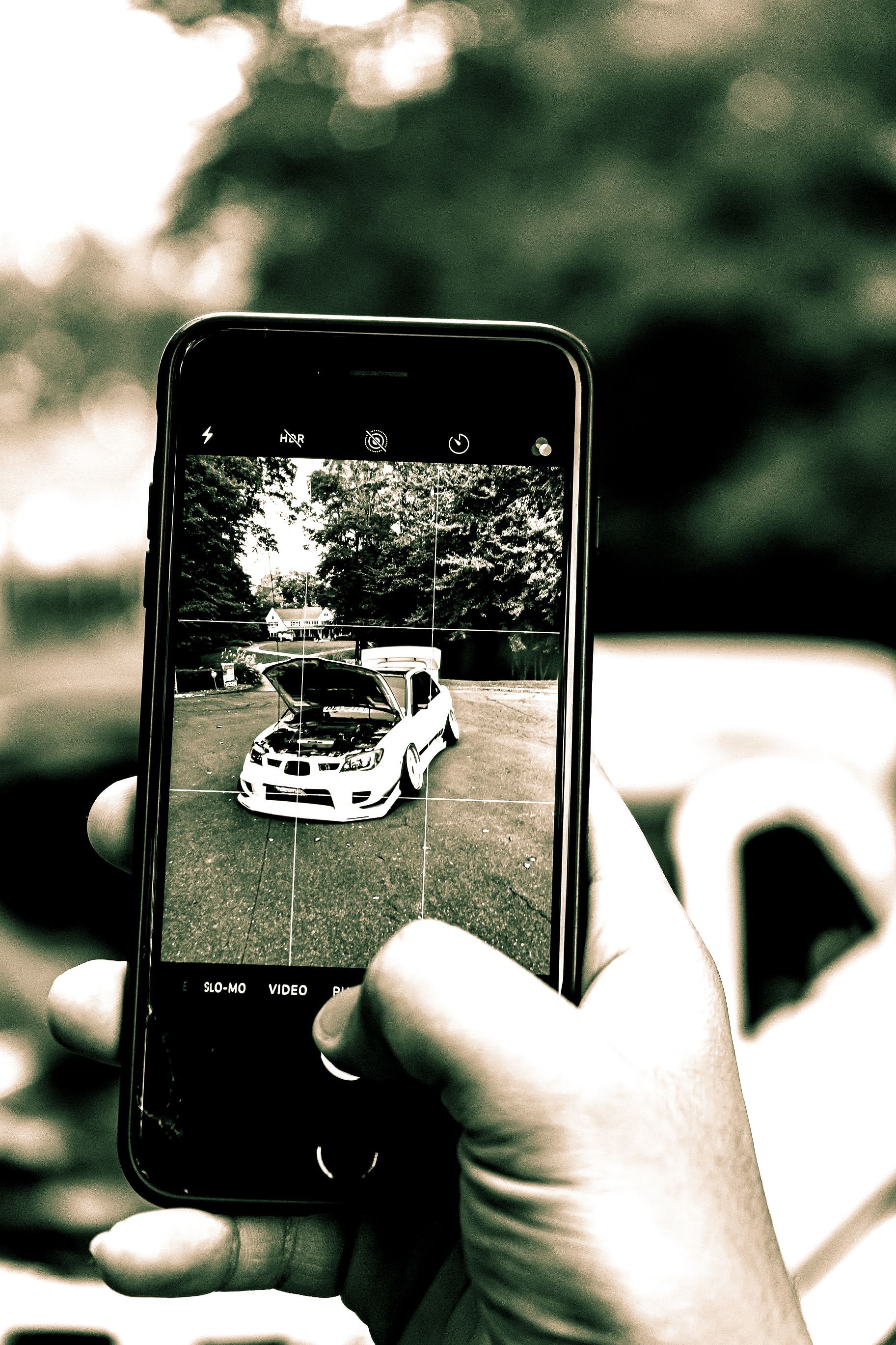 Person holding a smartphone taking a photo of a modified car with its hood open.