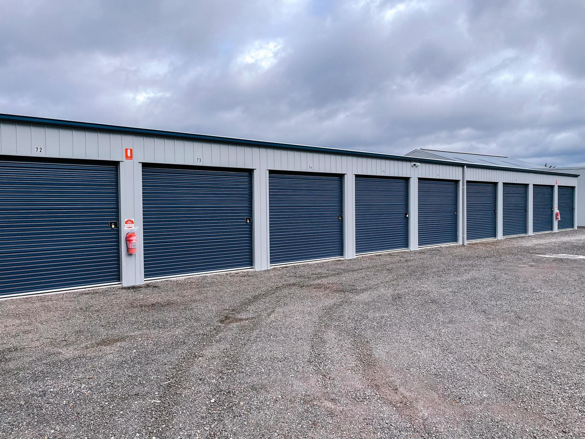 A row of blue garage doors are lined up in a gravel lot.
