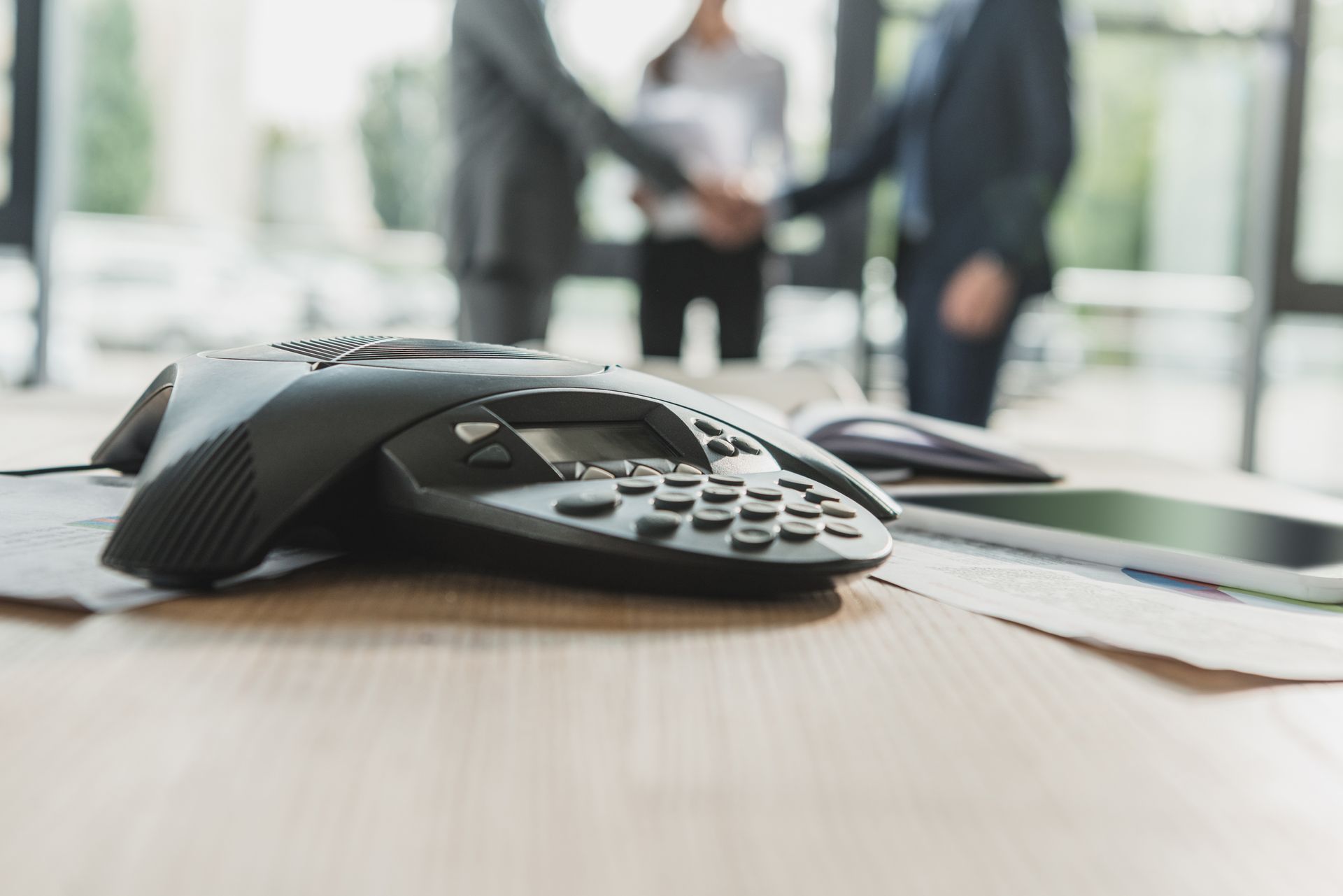 A telephone is sitting on a wooden table with two people shaking hands in the background.