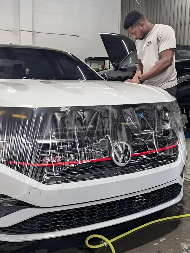 A man is wrapping a white car with plastic wrap in a garage.