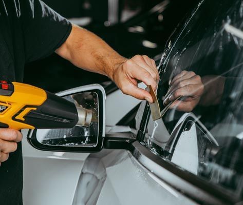A man is applying tinted glass to a car window.