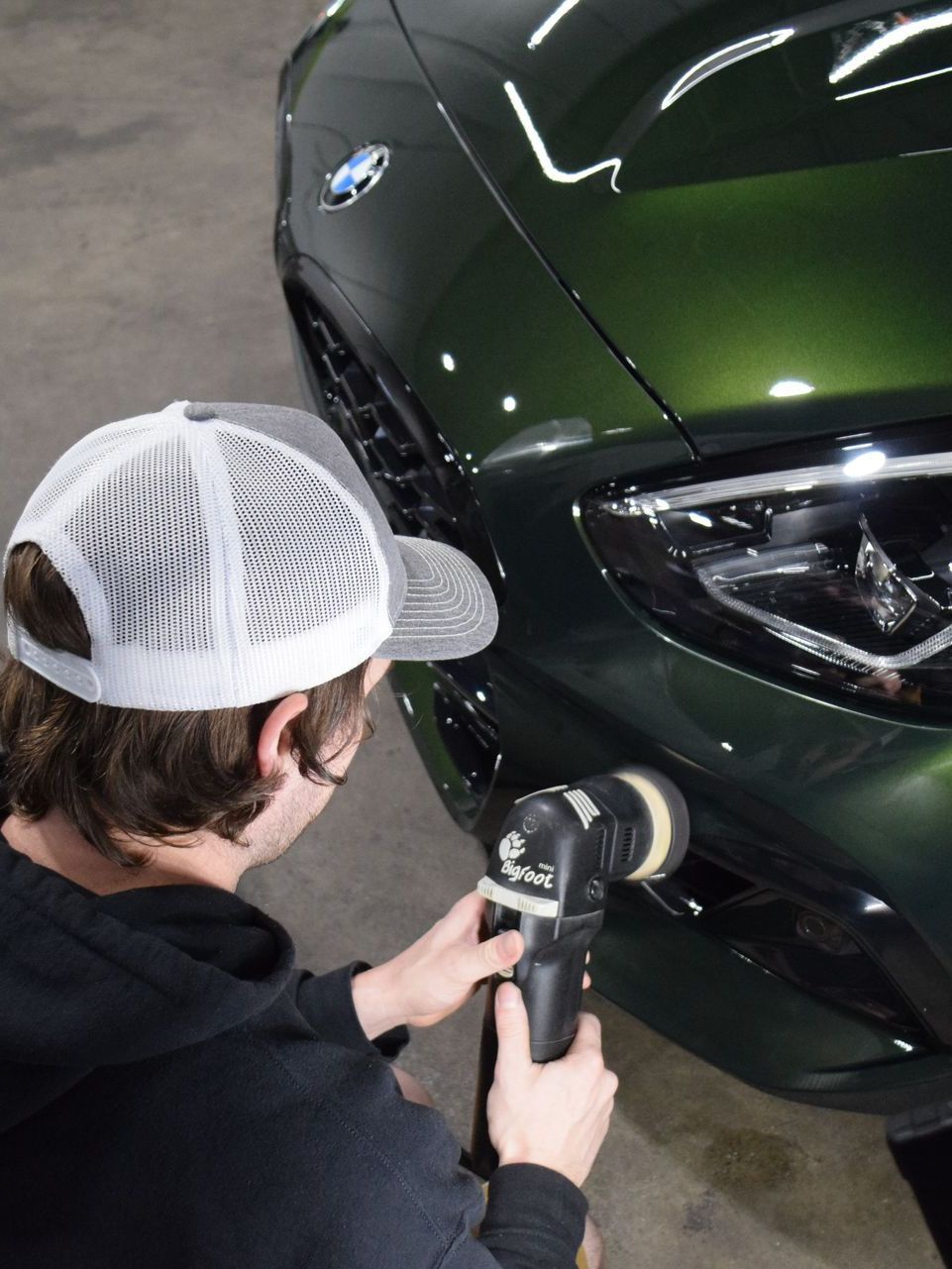 A man is polishing the front of a green car.