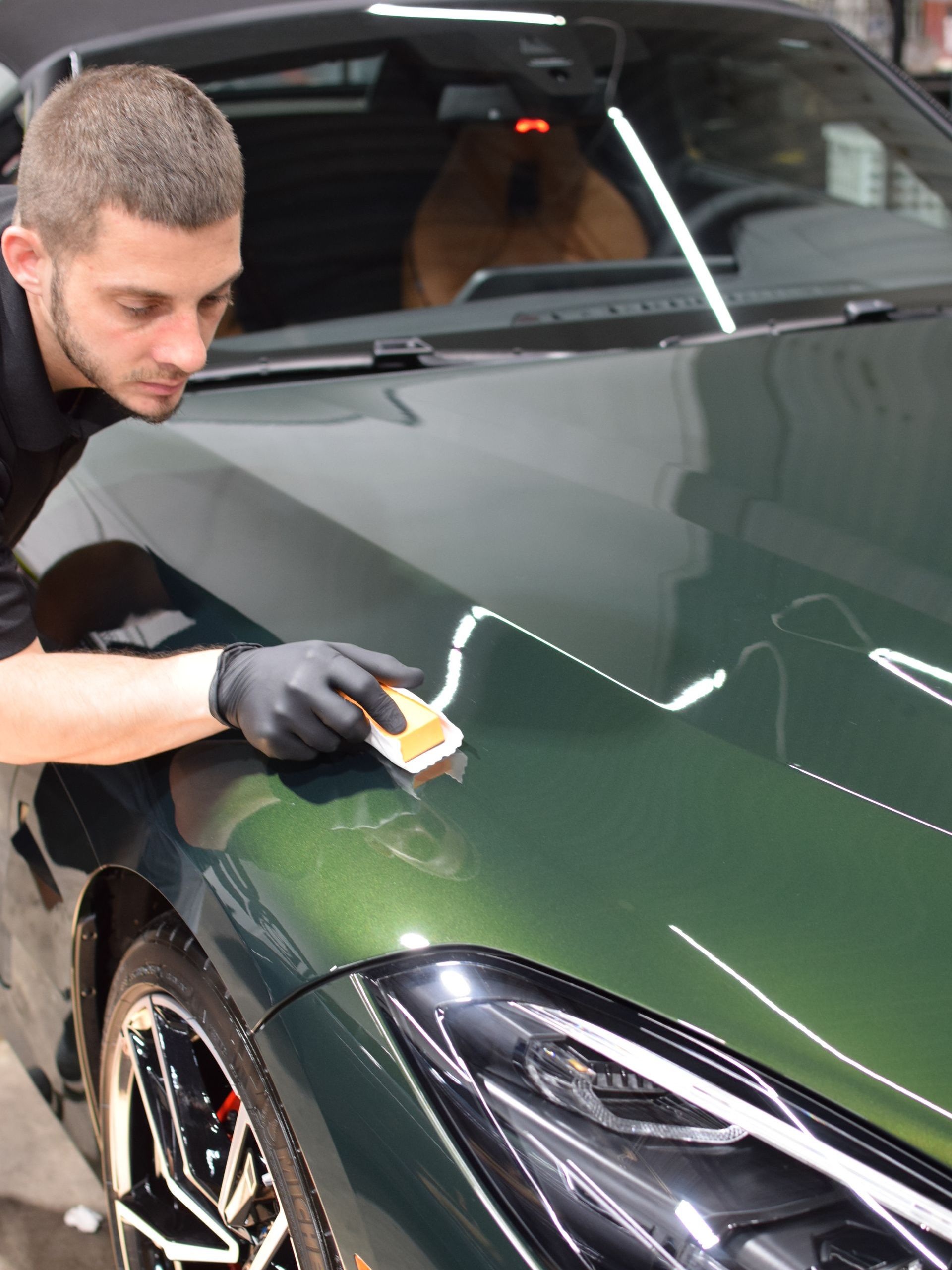 A man is polishing the hood of a green car