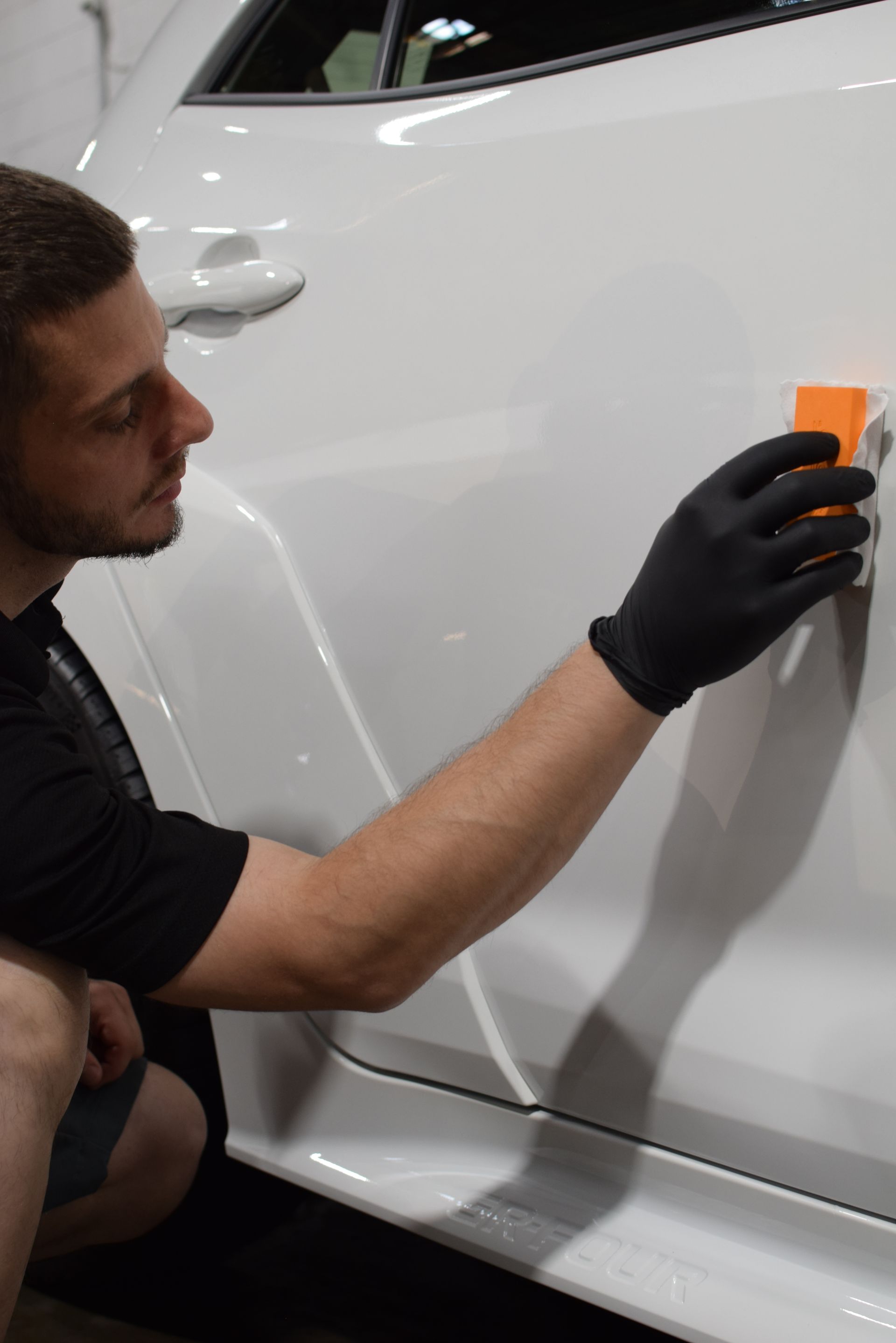 A man wearing black gloves is cleaning a white car with a sponge.