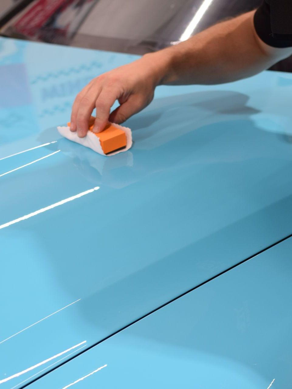 A person is cleaning a blue car with an orange sponge