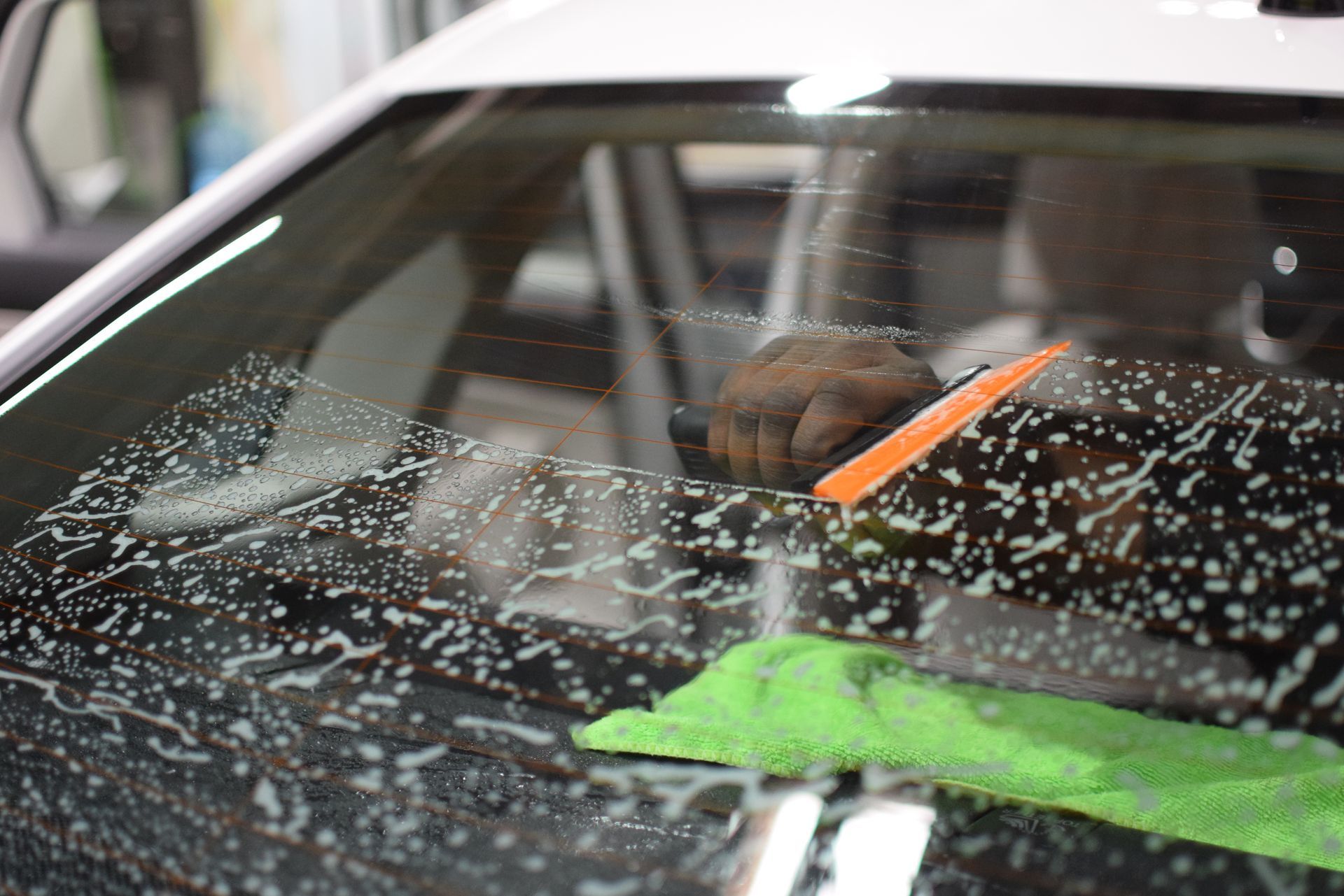 A person is cleaning the windshield of a car with a green cloth.