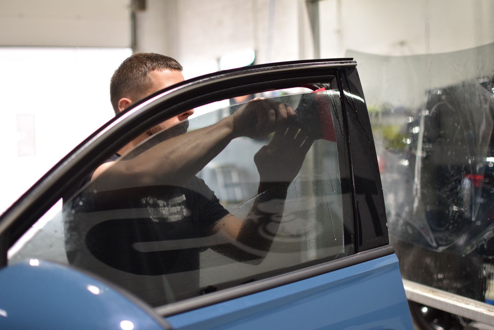 A man is installing window tinting on a blue car.
