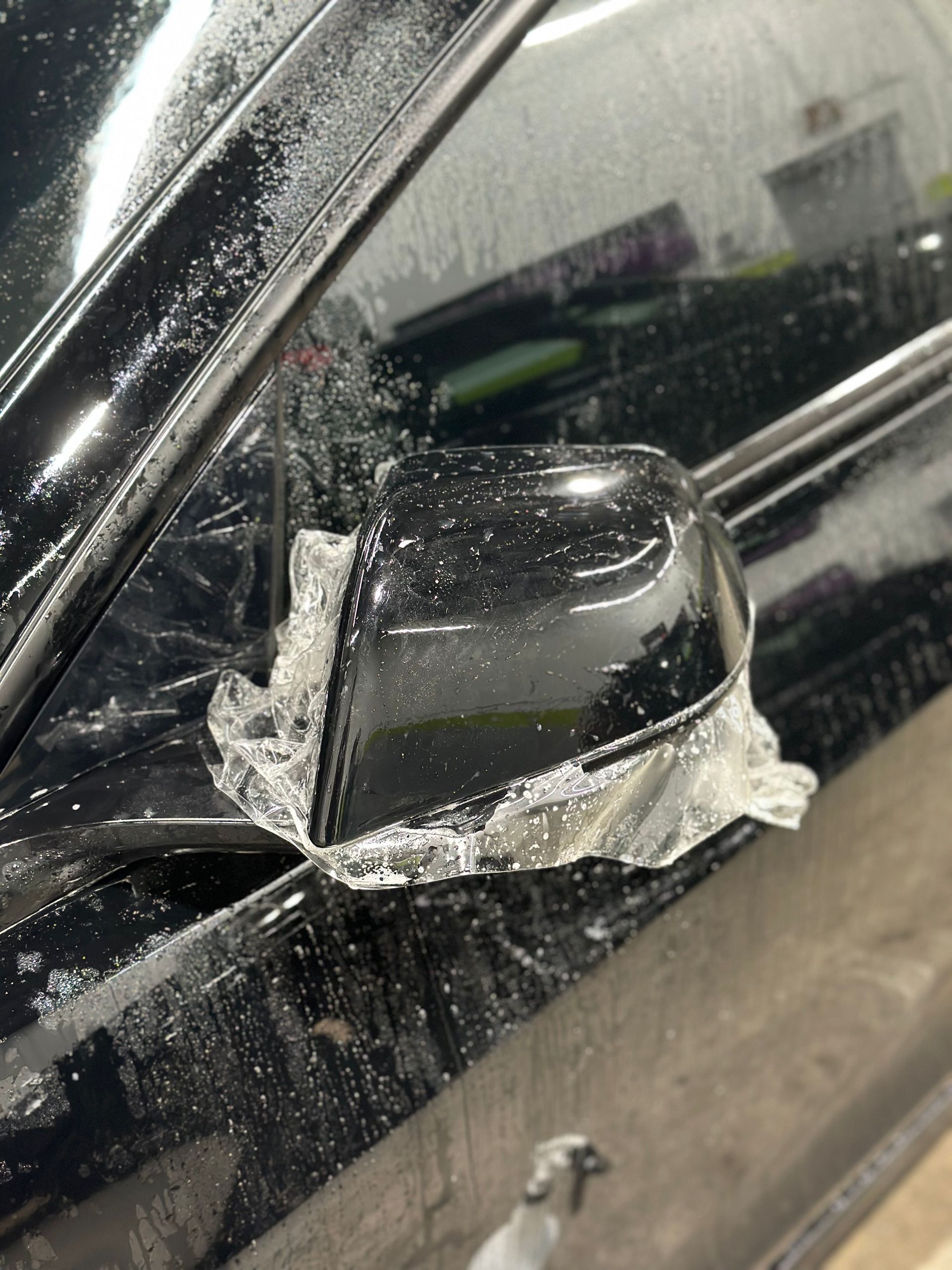 A black car with a side mirror covered in aluminum foil.