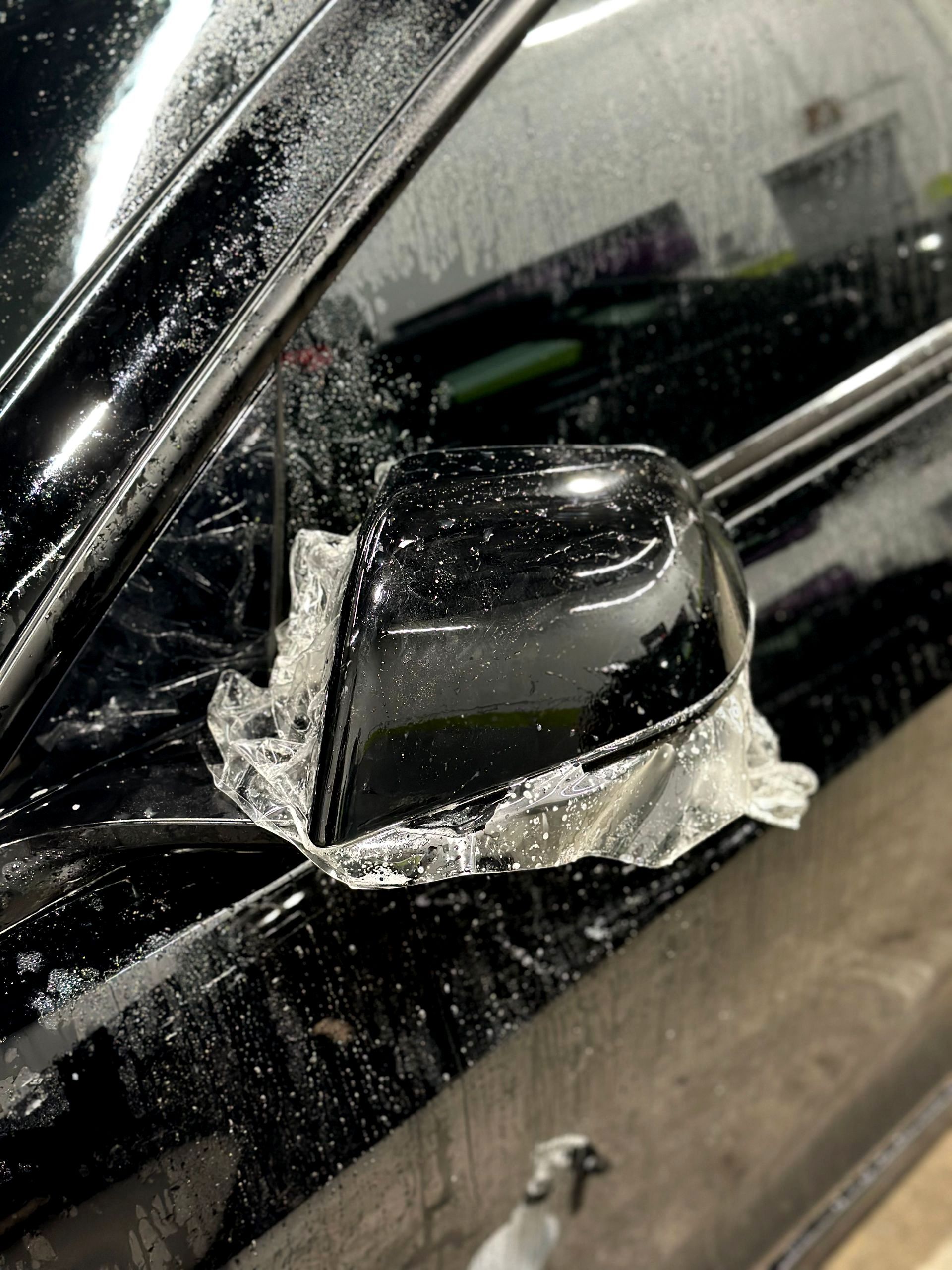 A black car with a side mirror covered in aluminum foil.