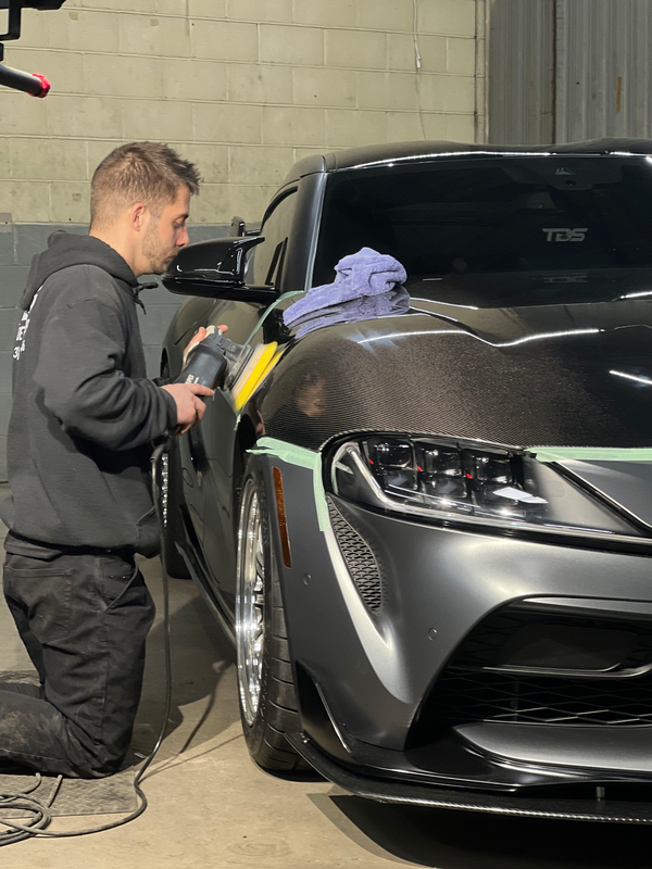 A man is kneeling down next to a car polishing it.
