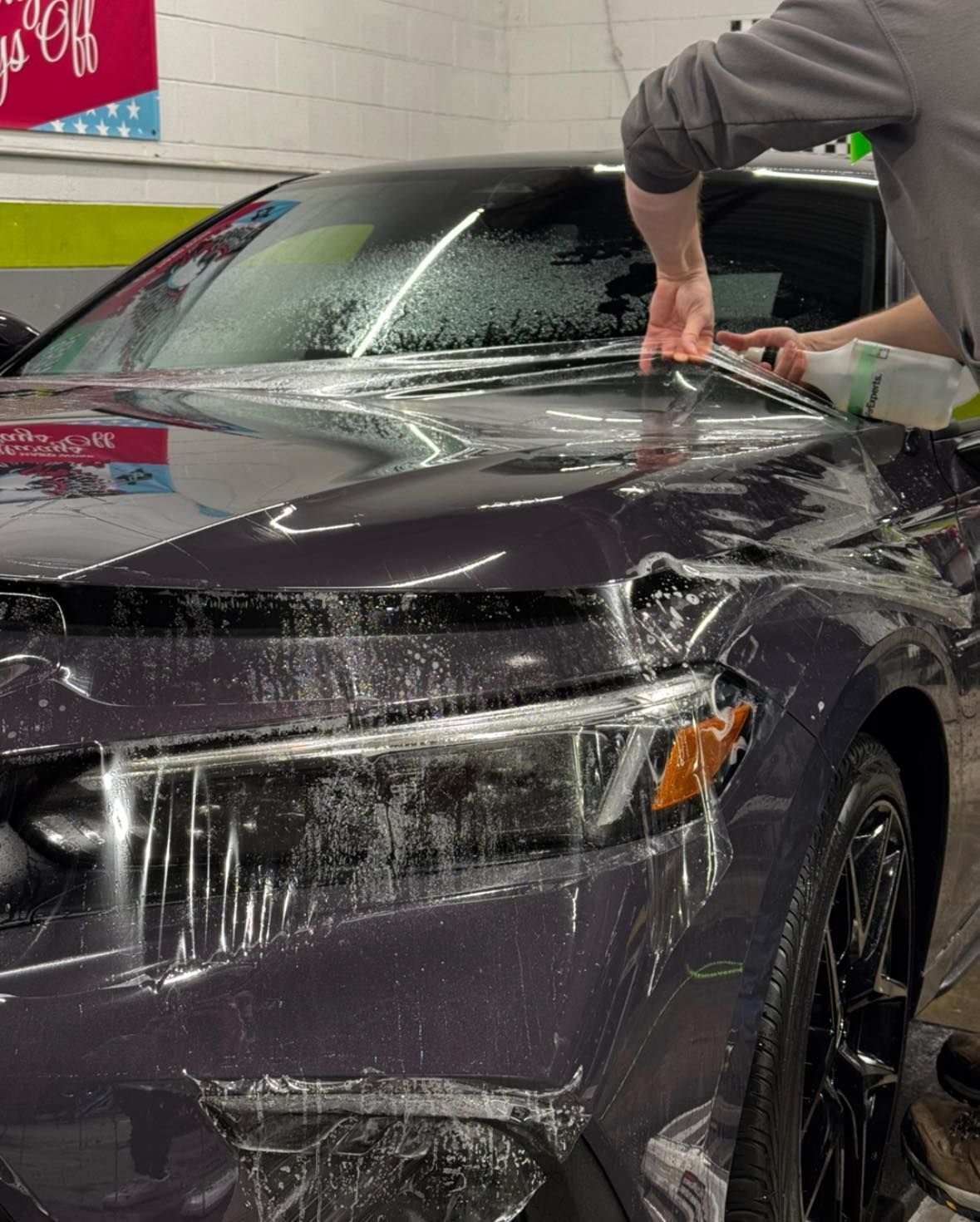 A man is cleaning the hood of a car with a spray bottle.