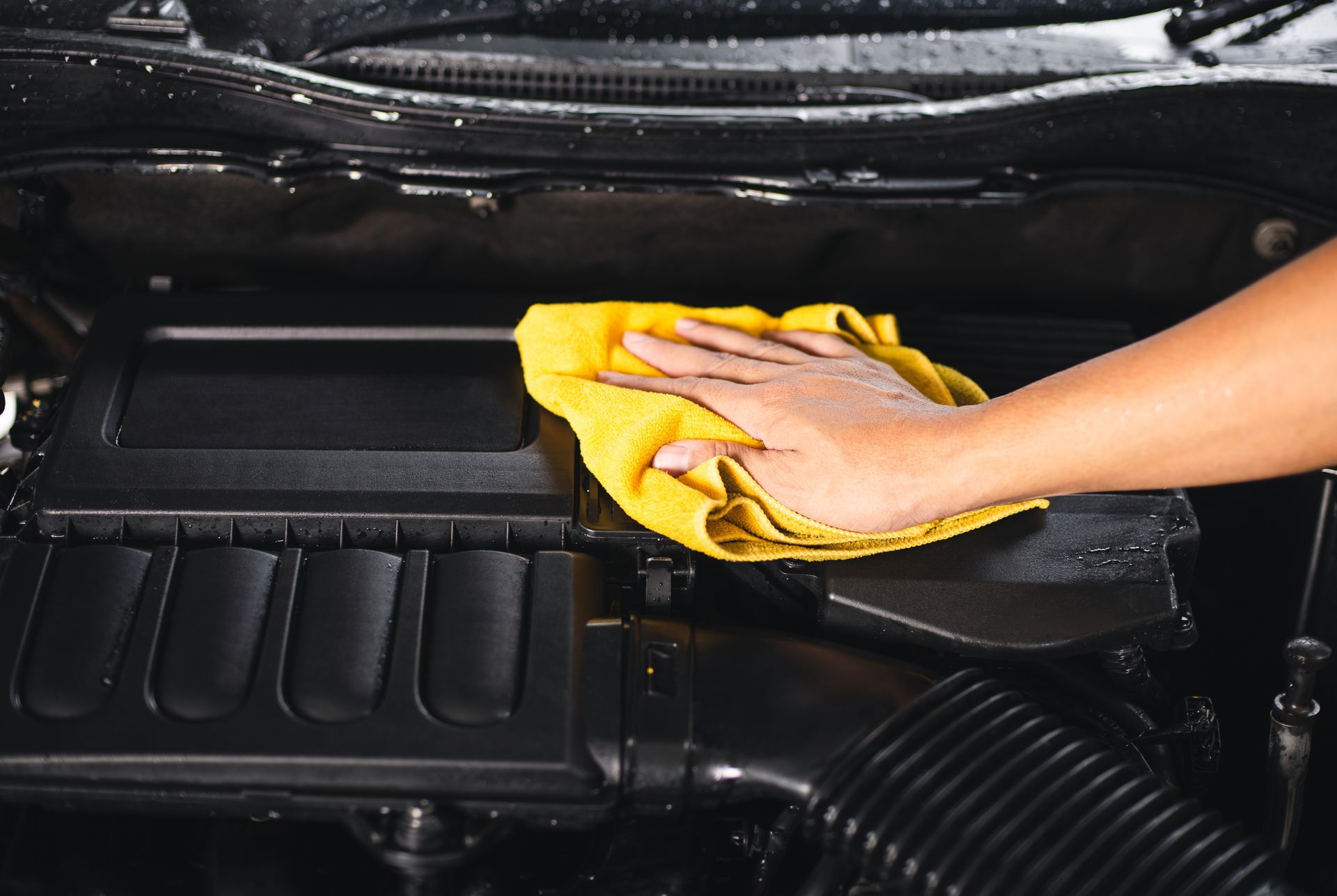A person is cleaning the engine of a car with a yellow towel.